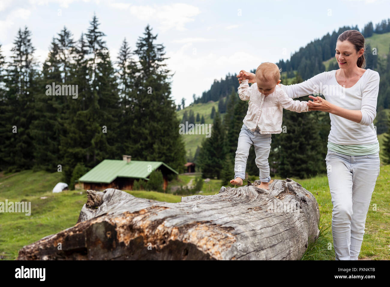 Germany, Bavaria, Oberstdorf, mother helping little daughter balancing on a log Stock Photo