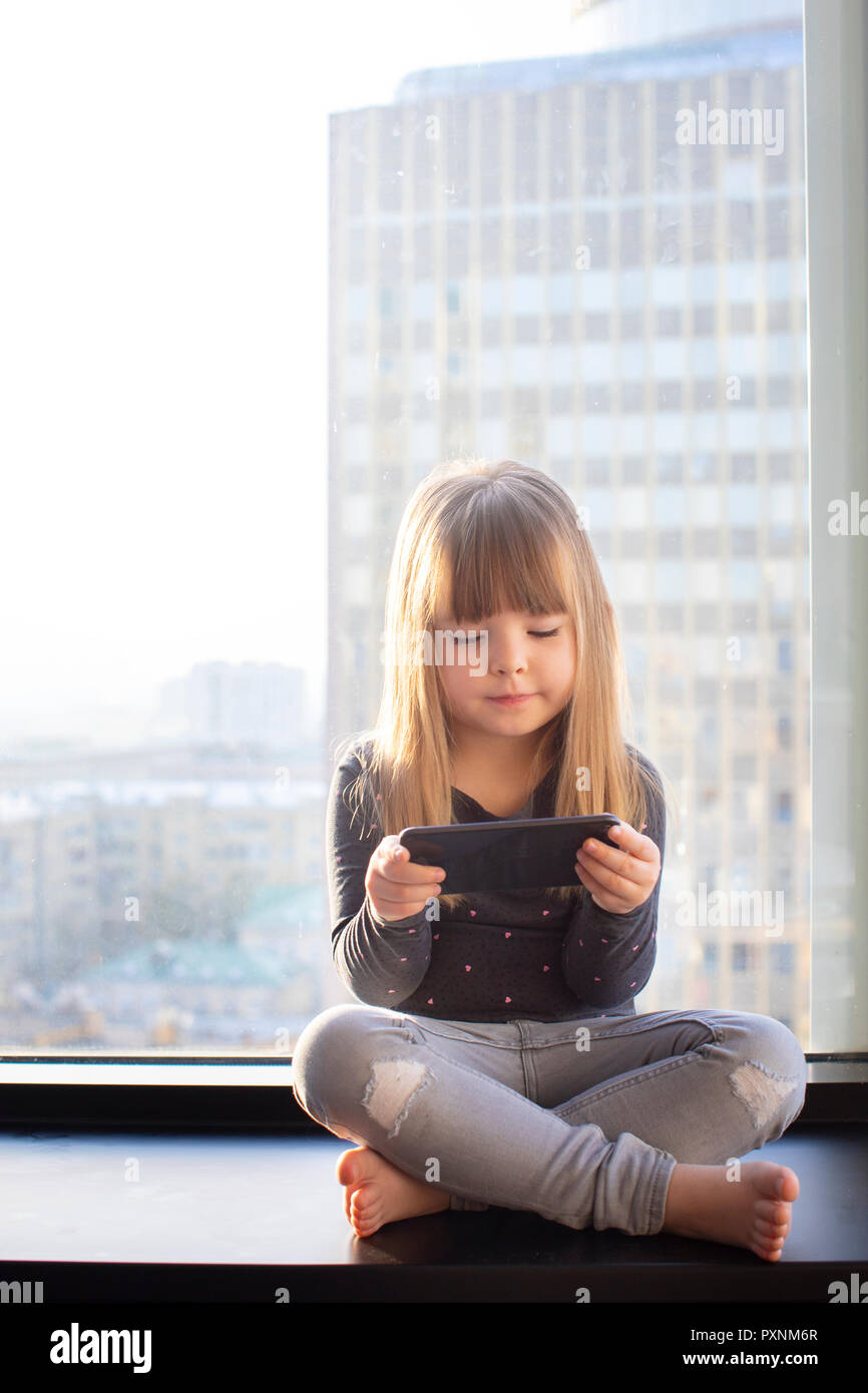 Cute little at home in white room is sitting near window. Stock Photo