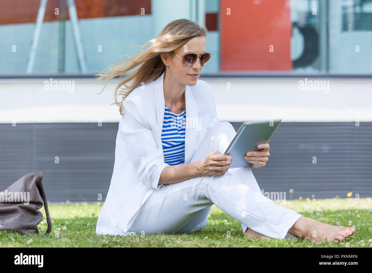 Smiling blond businesswoman using tablet sitting on meadow Stock Photo