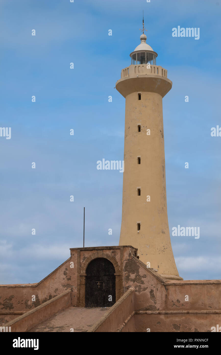 Light color of the tower of lighthouse. Fence with an old gate with an arc. Cloudy sky. Rabat, Morocco. Stock Photo