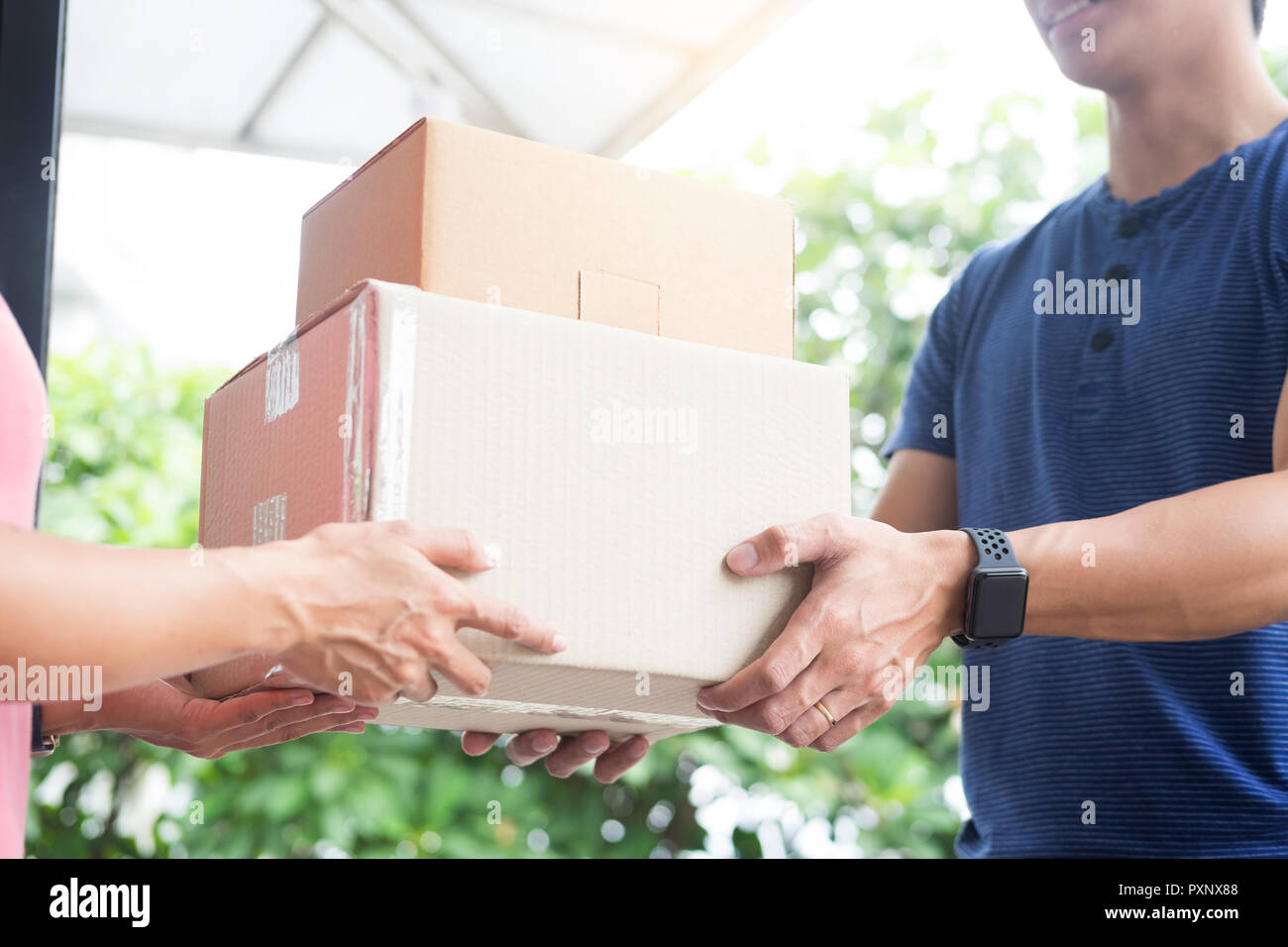 woman courier holding a parcel Shipping Mail appending signature signing delivery note after receiving package from delivery man. Stock Photo