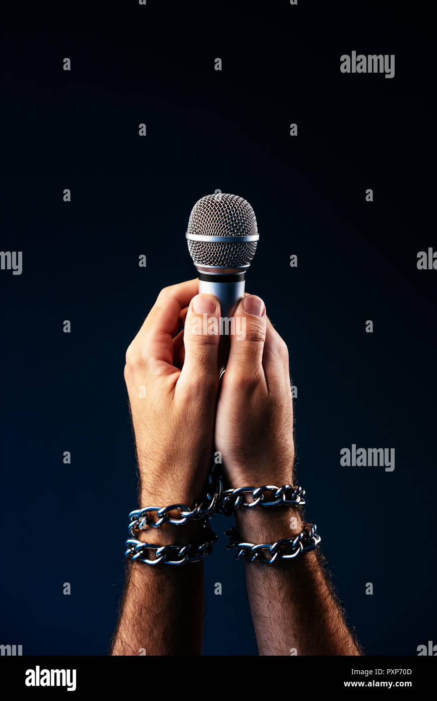 Freedom of the press and journalism, conceptual image with microphone in male hand tied with chains, low key image Stock Photo
