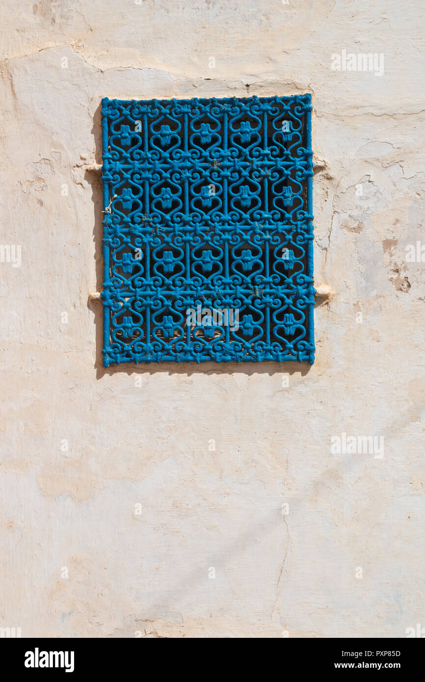 Structured old wall, enlightened by the sunlight. Typical blue moroccan color of the ornamental grid in the window. Kasbah de Oudaias, Rabat, Morocco Stock Photo