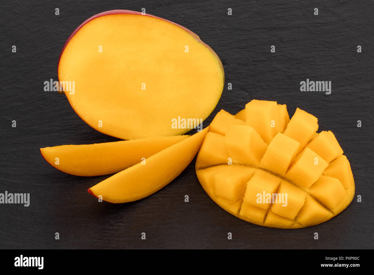 ripe mango cut in half and diced on dark slate Stock Photo Alamy