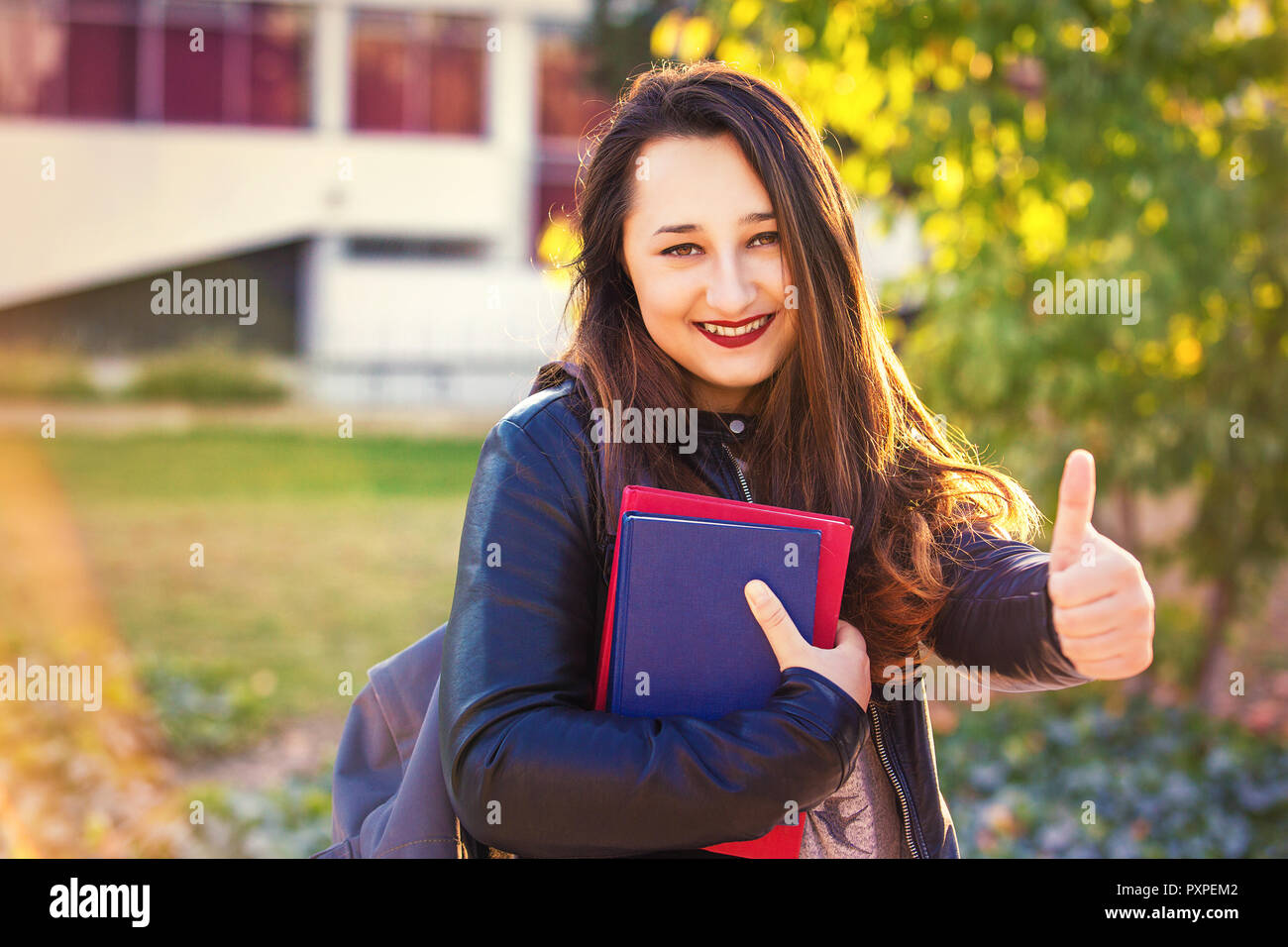 Joyful young girl student show thumb up gesture holding books and smile ...