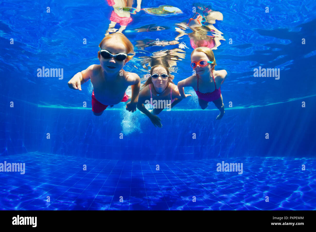 Happy family - mother, baby son, daughter in goggles swim, dive in pool with fun - jump deep down underwater. Healthy lifestyle, water sport activity Stock Photo