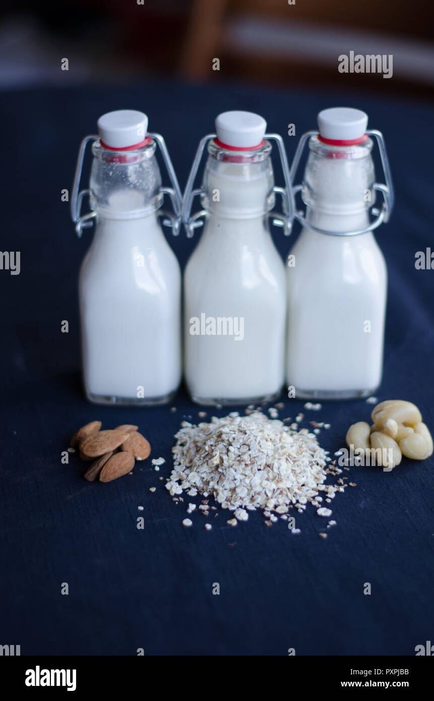 Almond milk, cashew nut milk and oat milk standing together with ingredients in front. Stock Photo