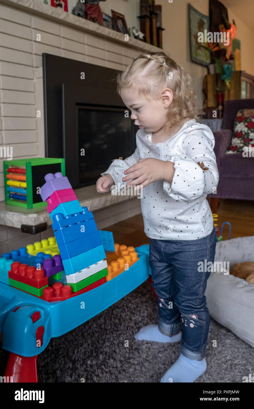 Almost 2 year old girl at play with blocks she has stacked, unsure of what to do as they are just about to fall over. Stock Photo