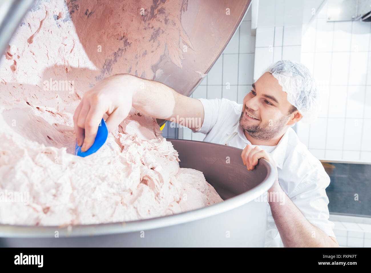 Butcher grounding meat in grinder machine to make sausages Stock Photo