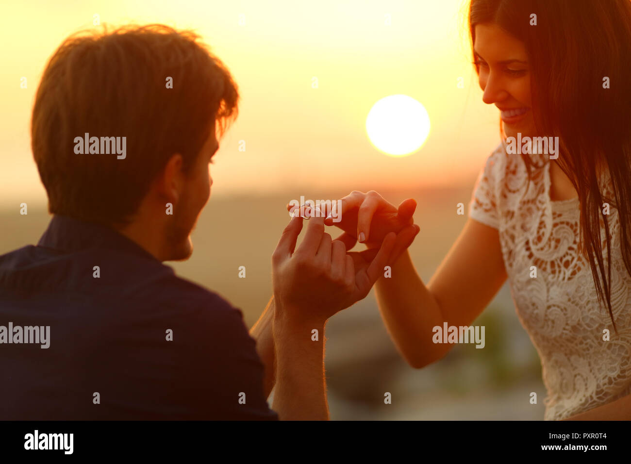 Happy man putting engagement ring in girlfriend finger at sunset on the