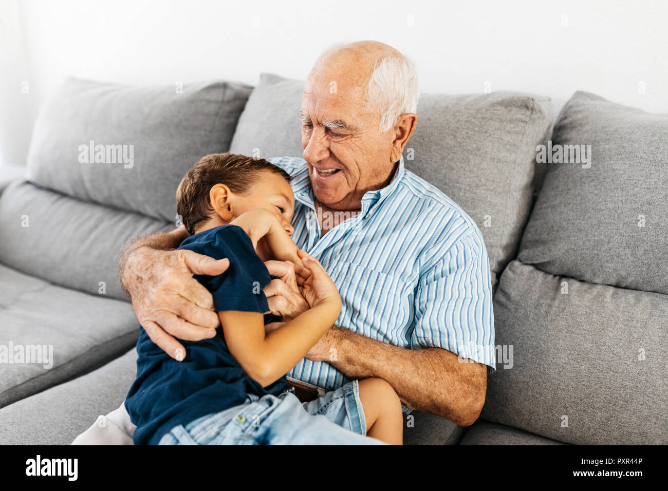 Grandson and grandfather laughing while tickling each other on the couch Stock Photo