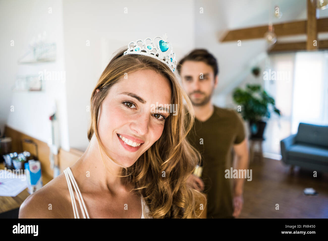 Portrait of smiling woman wearing tiara at home with man in background Stock Photo