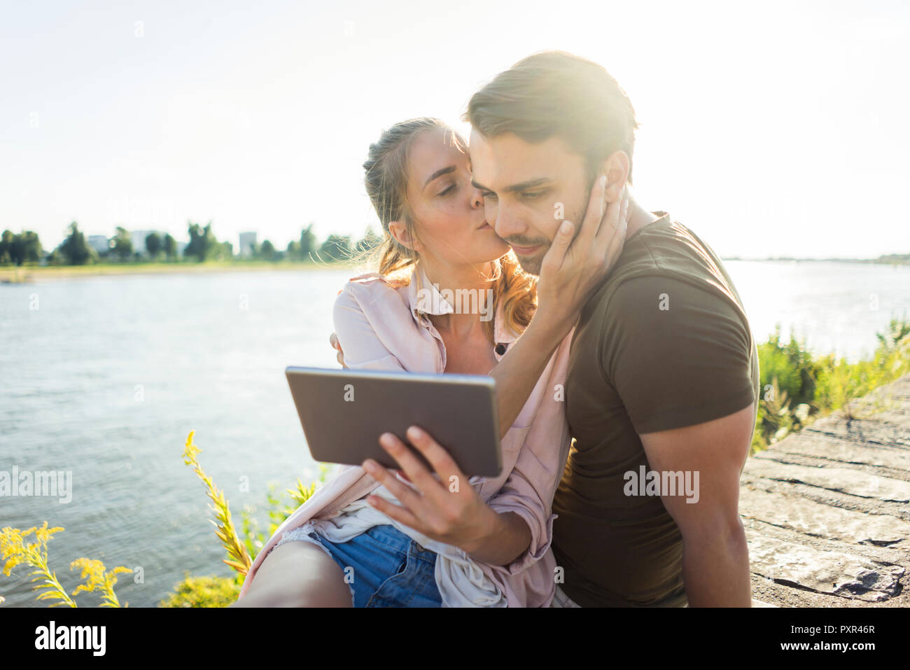 Couple kissing at the riverside in summer holding tablet Stock Photo ...