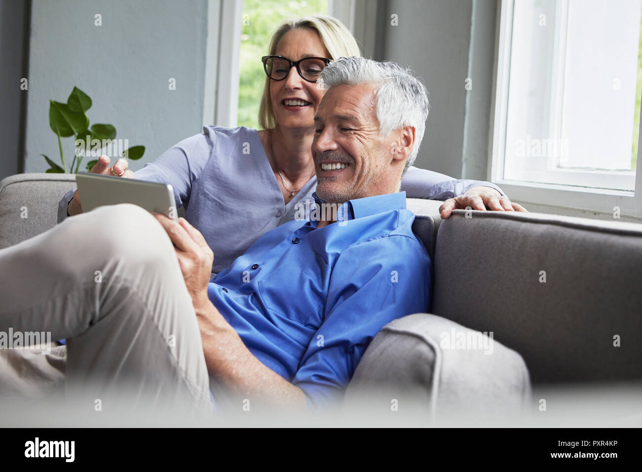 Happy mature couple sitting on couch at home sharing tablet Stock Photo