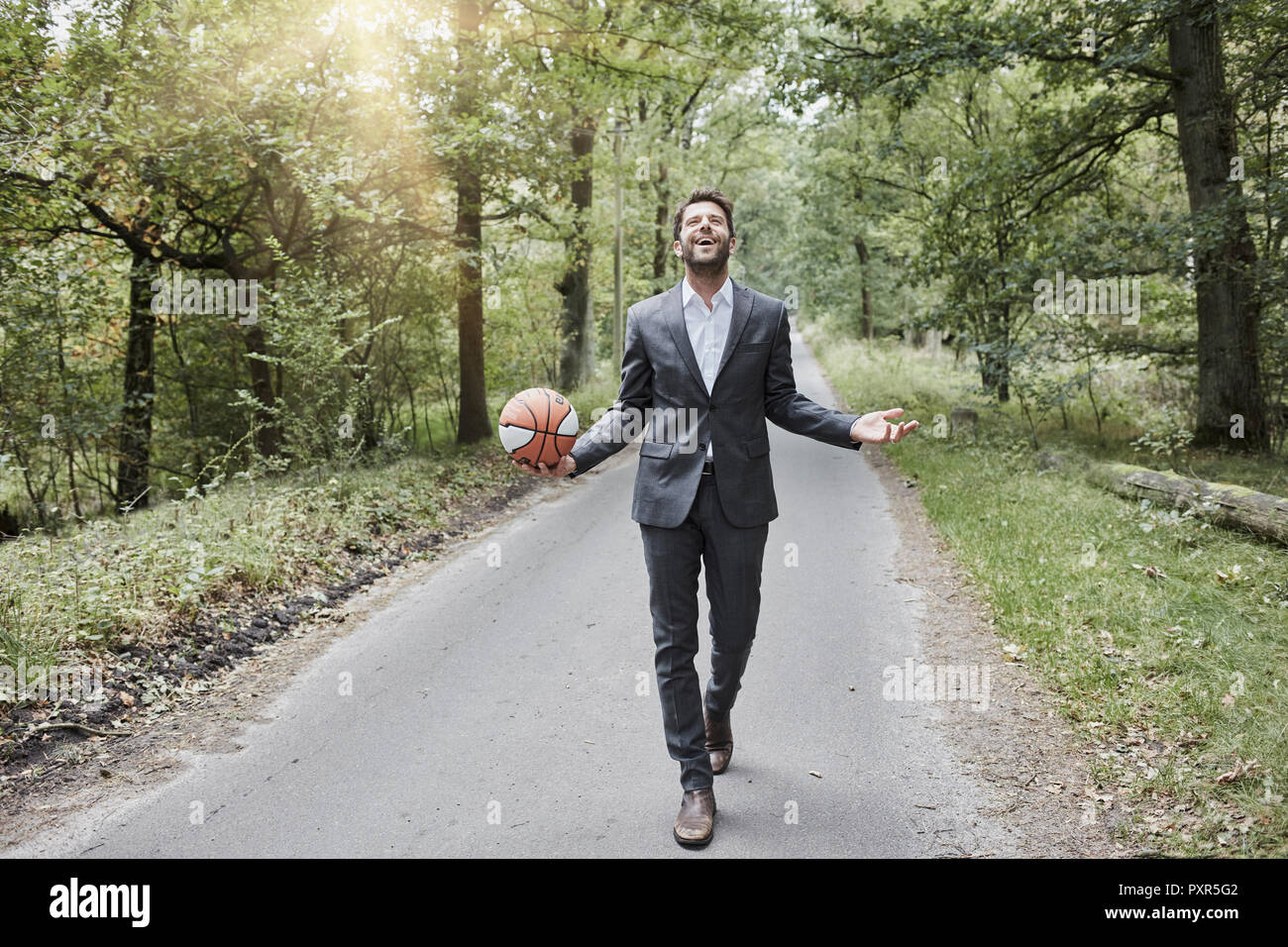 Happy businessman walking with basketball on rural road Stock Photo