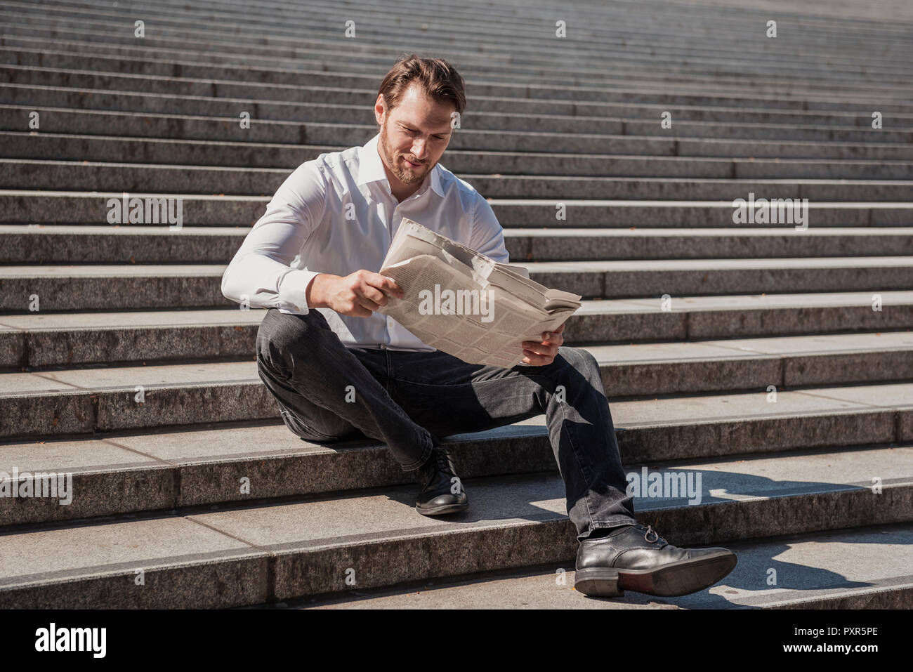 Smiling businessman sitting on stairs reading newspaper Stock Photo