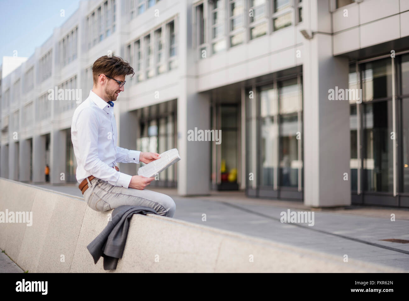 Businessman sitting in the city reading newspaper Stock Photo