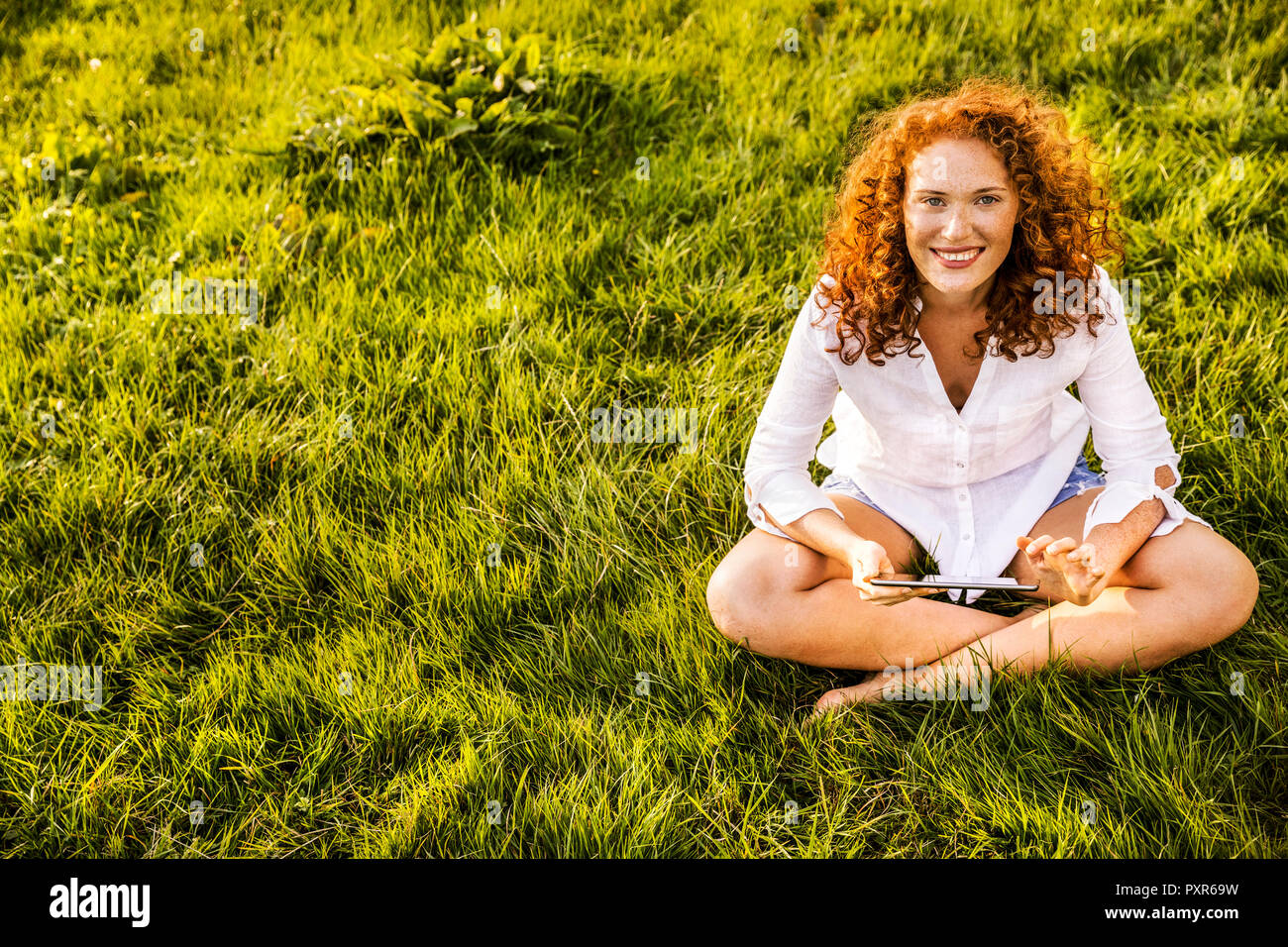 Portrait of happy young woman with tablet relaxing on a meadow Stock Photo