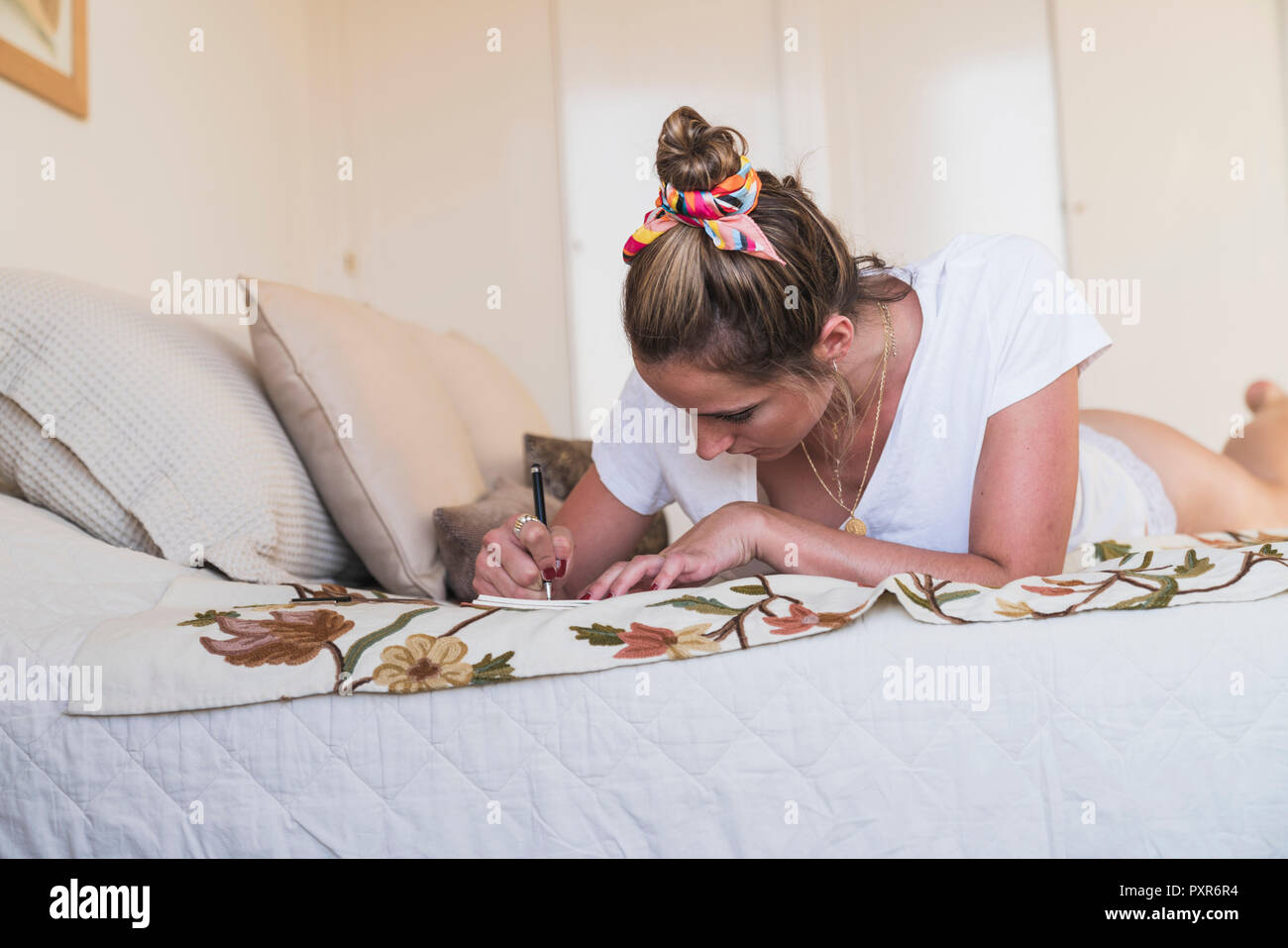 Young woman lying on bed at home writing in diary Stock Photo