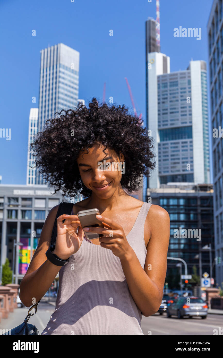 Germany, Frankfurt, portrait of smiling young woman with curly hair using cell phone Stock Photo