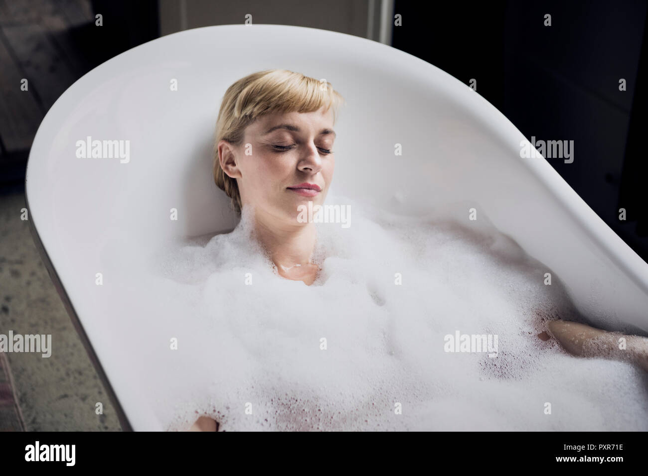 Portrait of woman with eyes closed taking bubble bath in a loft Stock Photo