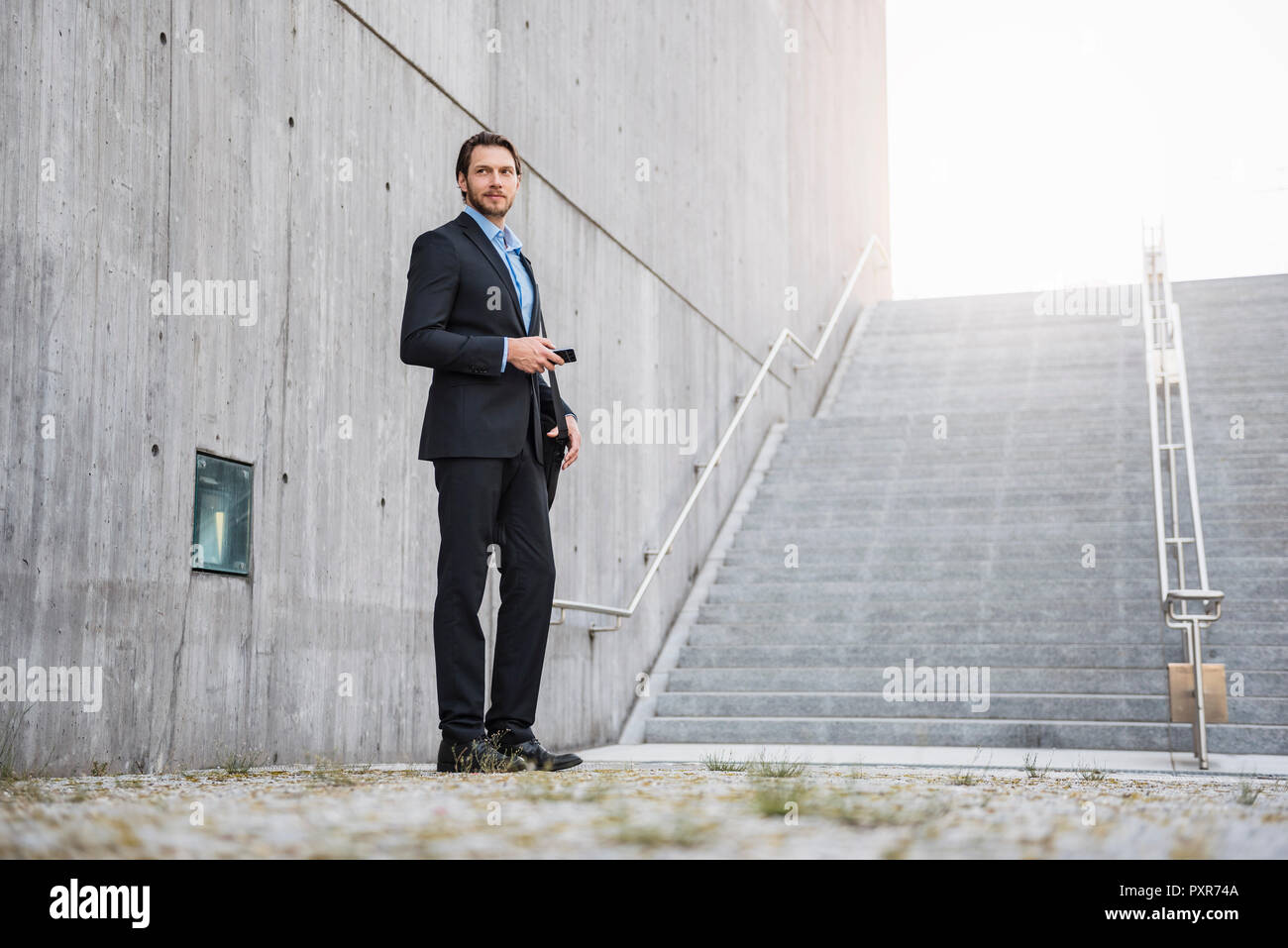 Businessman standing at stairs holding smartphone Stock Photo - Alamy