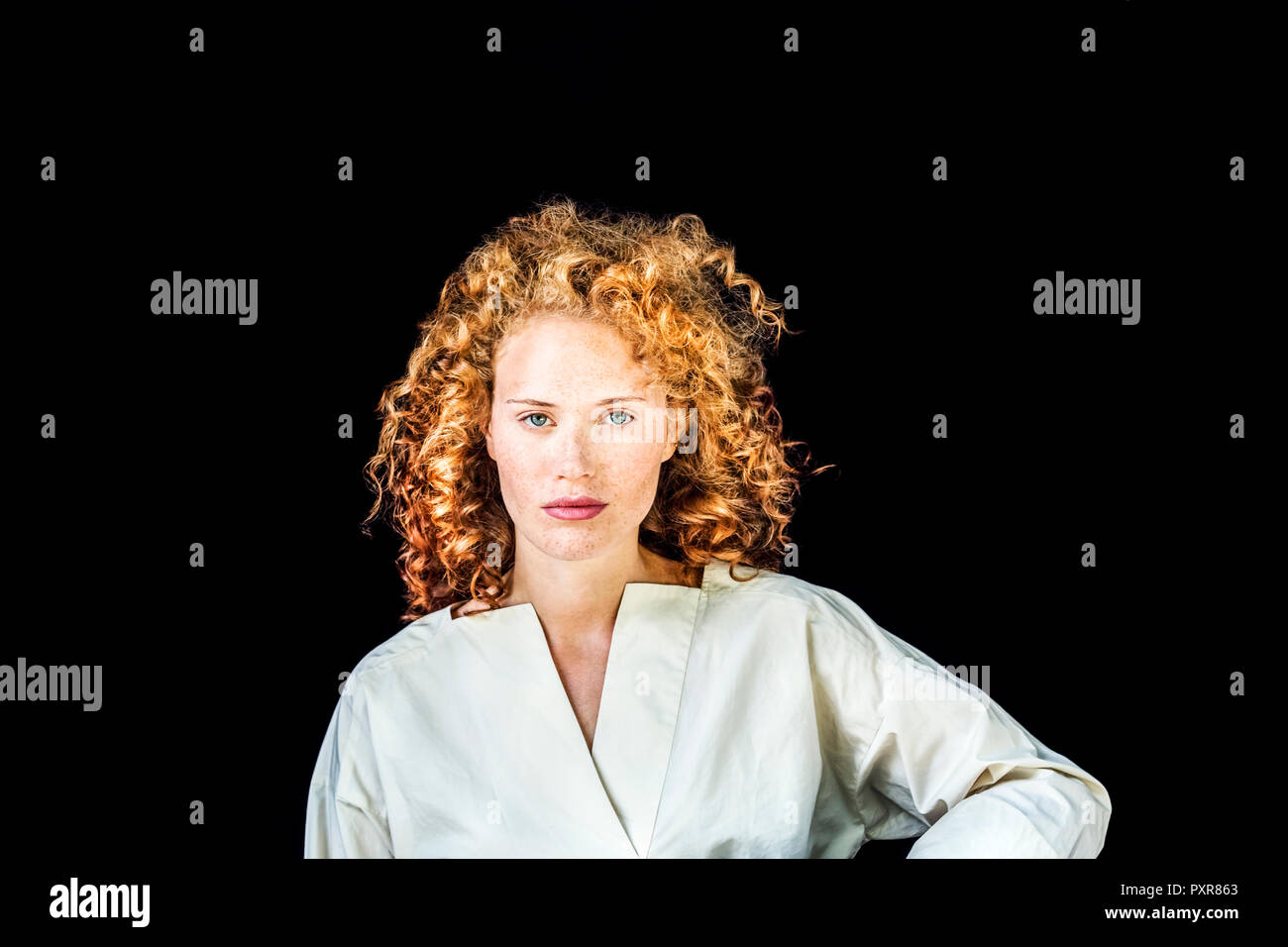 Portrait of serious young woman with curly red hair in front of black background Stock Photo