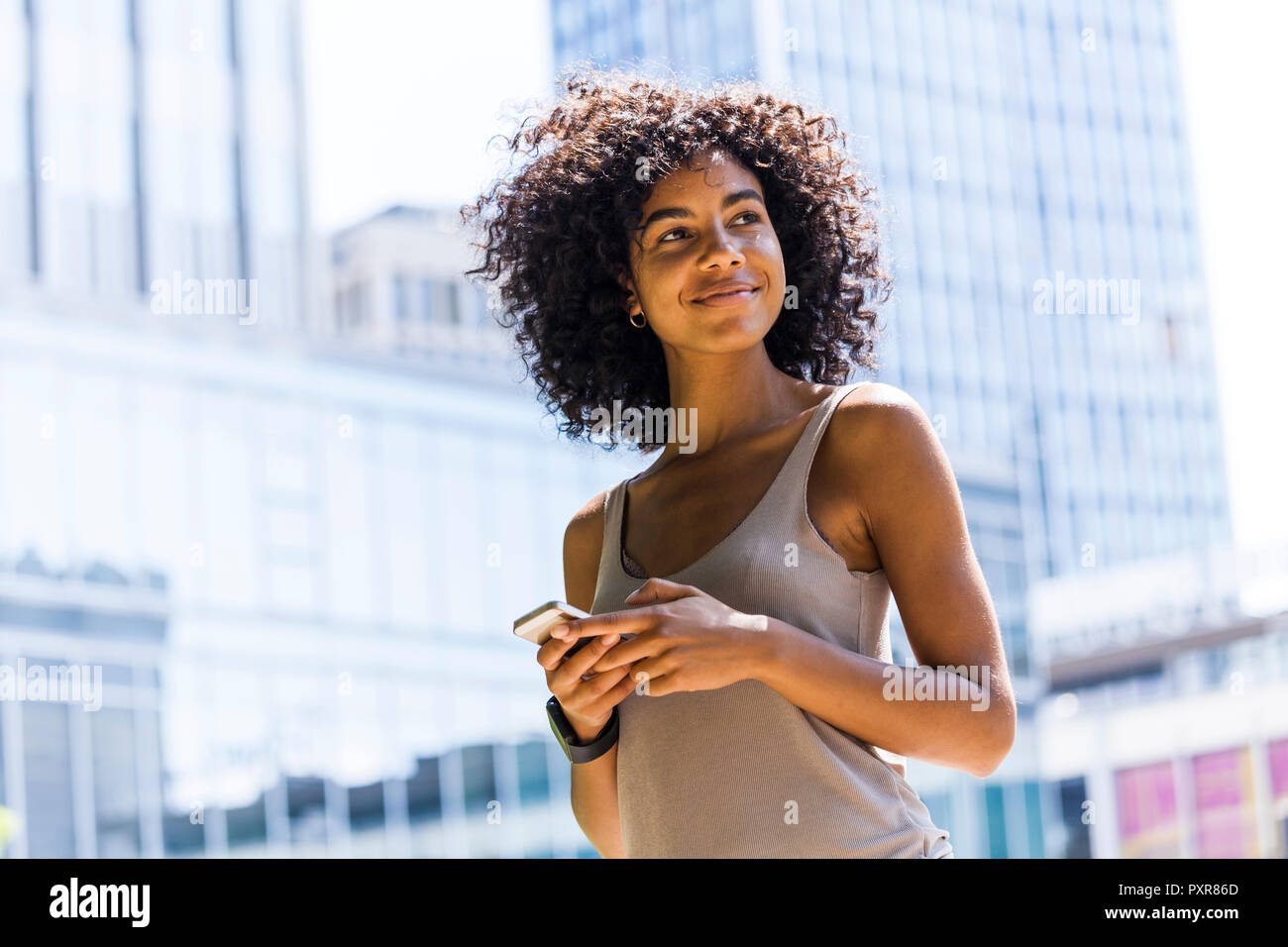 Germany, Frankfurt, portrait of smiling young woman with curly hair in front of skyscrapers Stock Photo