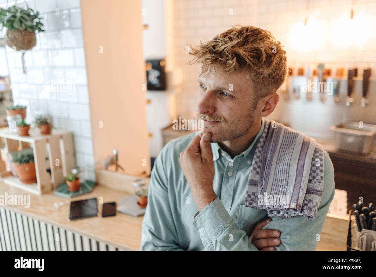 Young man working in his start-up cafe, thinking Stock Photo