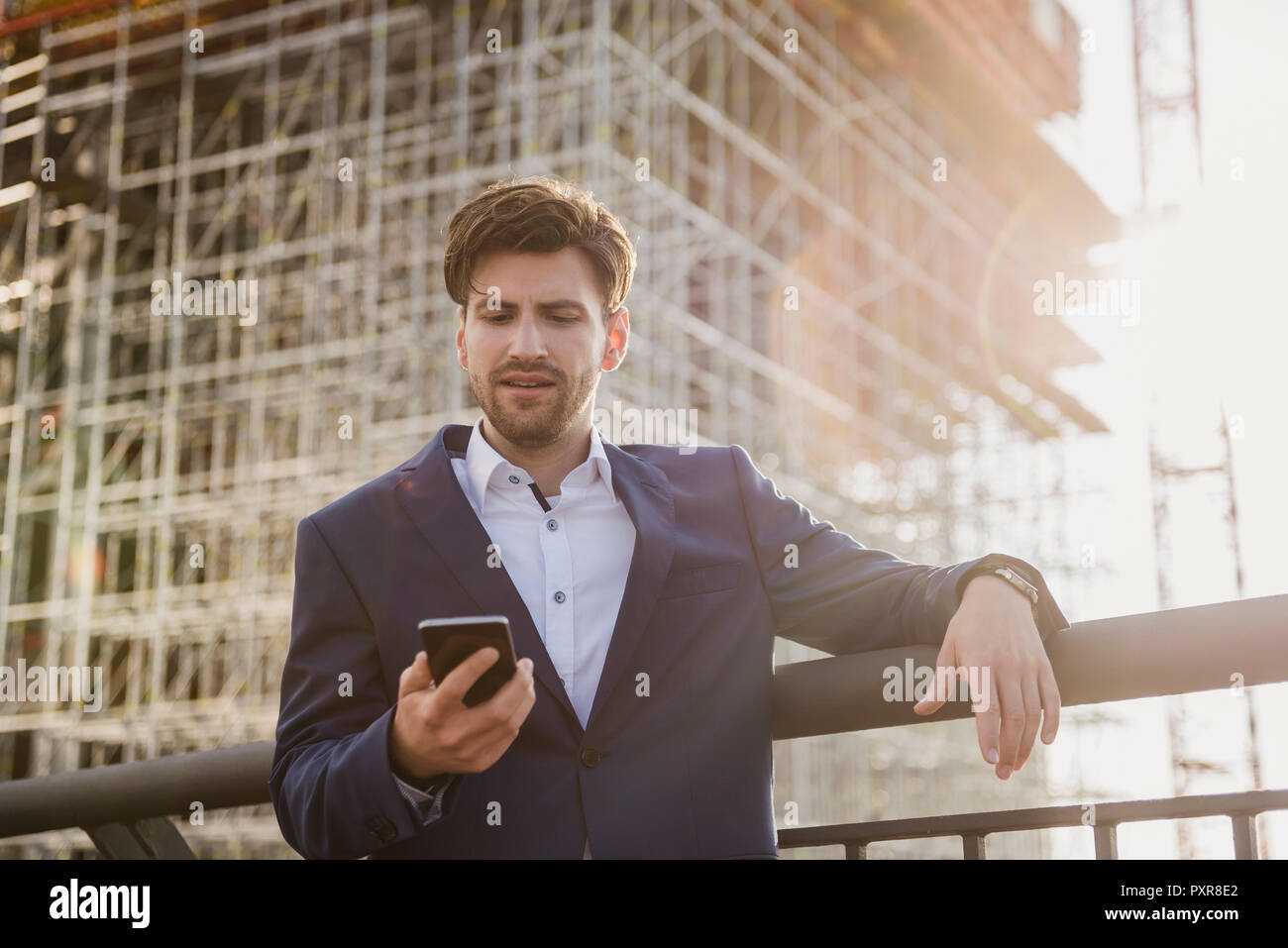 Businessman standing on bridge in front of construction site using cell phone Stock Photo