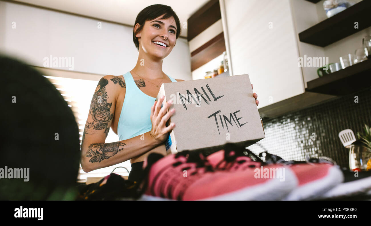 Smiling young woman looking at camera with fan mail box in hand. Female vlogger making mail time video at home Stock Photo