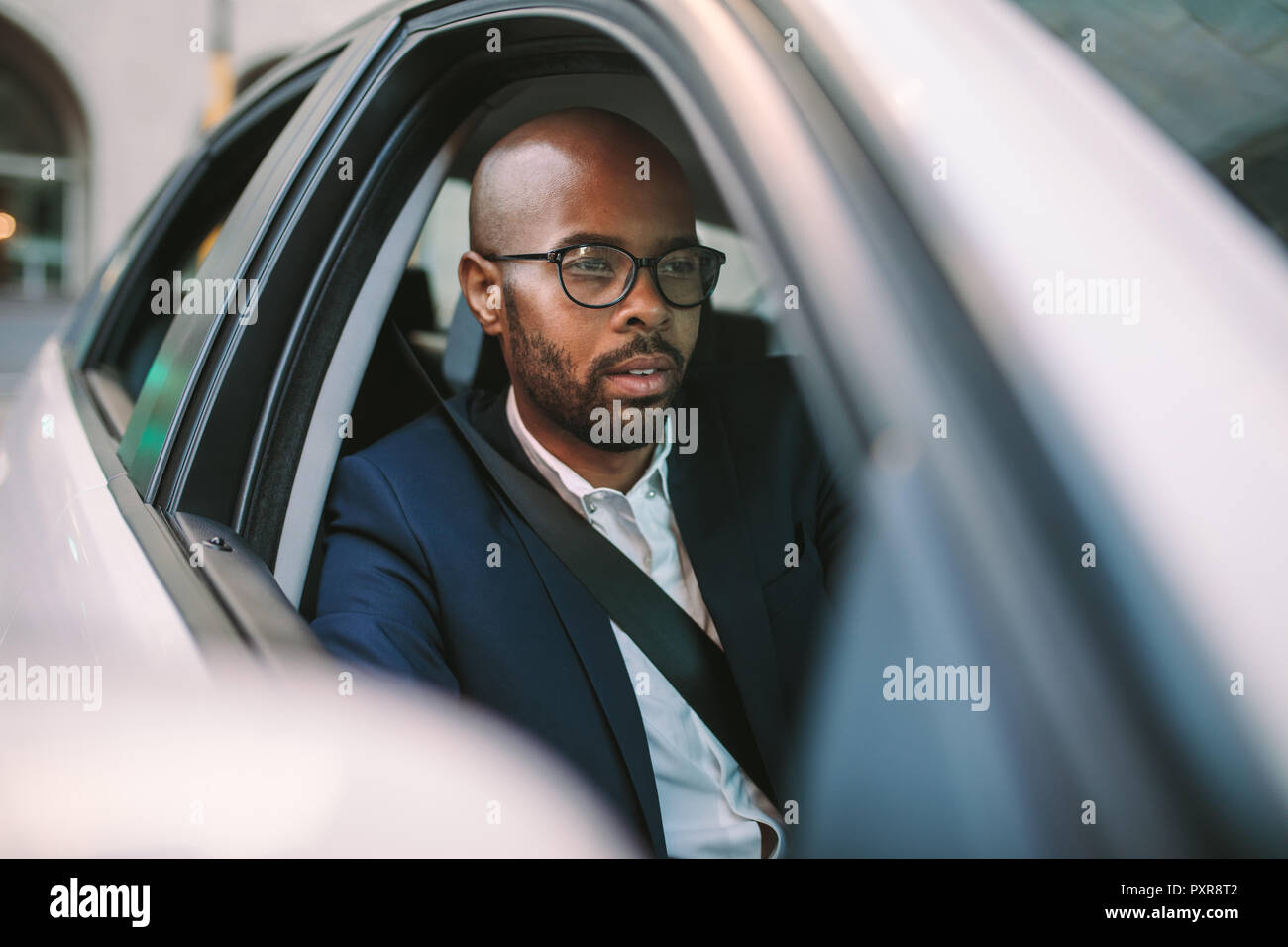 African businessman driving a car to office. Bald male concentrating on road while driving a car. Stock Photo