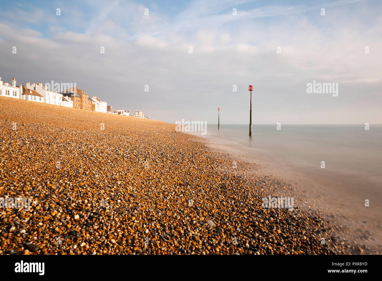 Early morning light on the shingle beach at Deal, Kent, UK. The houses along Beach Street are visible and there are tidal markers in the sea. Stock Photo