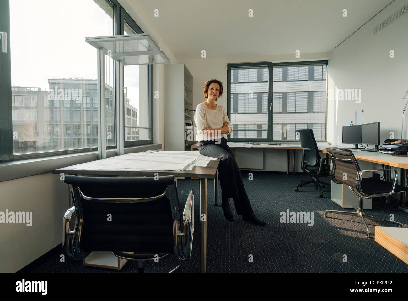 Successful businesswoman sitting on desk in her office Stock Photo - Alamy