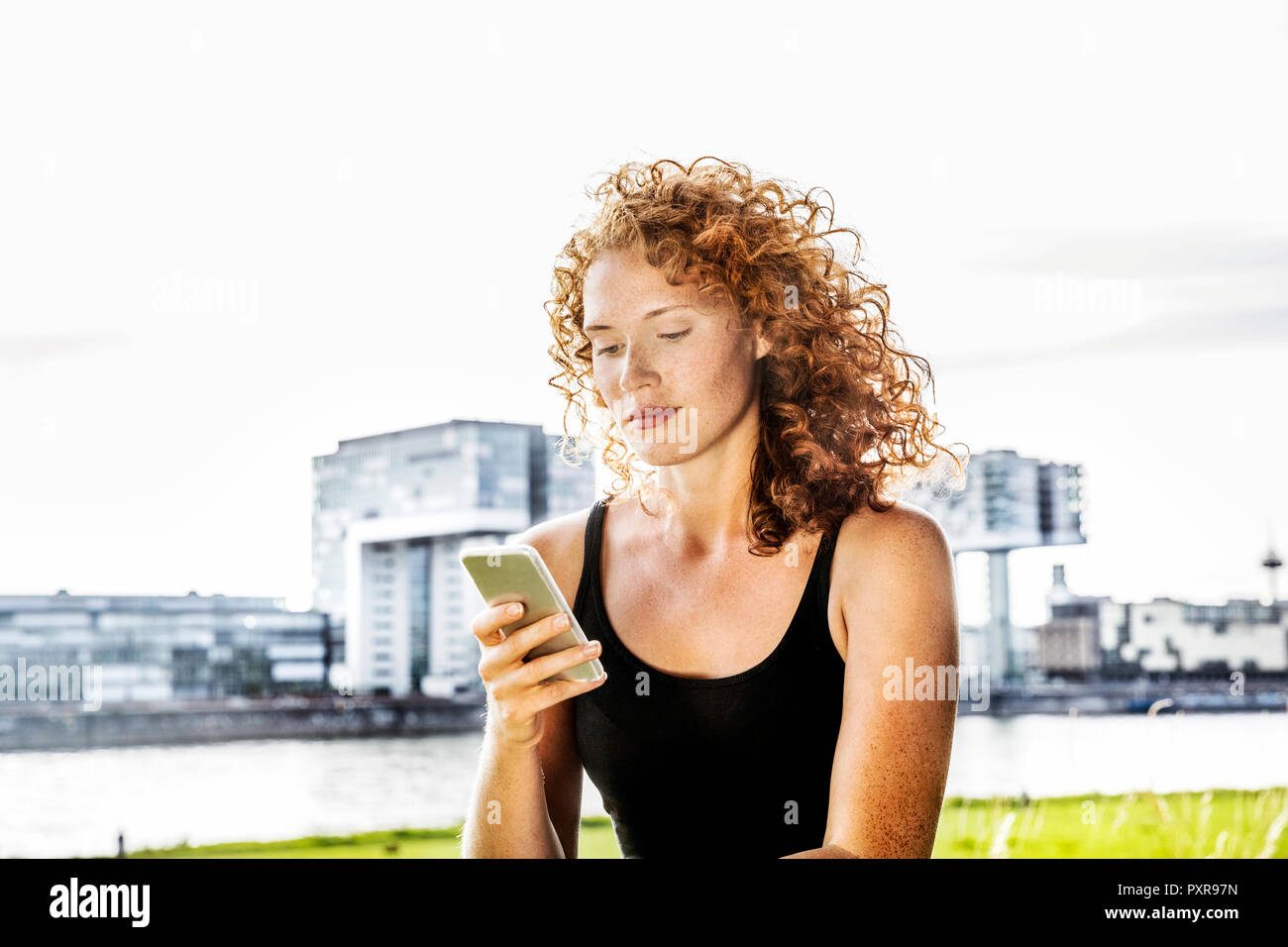 Germany, Cologne, portrait of serious young woman looking at cell phone Stock Photo