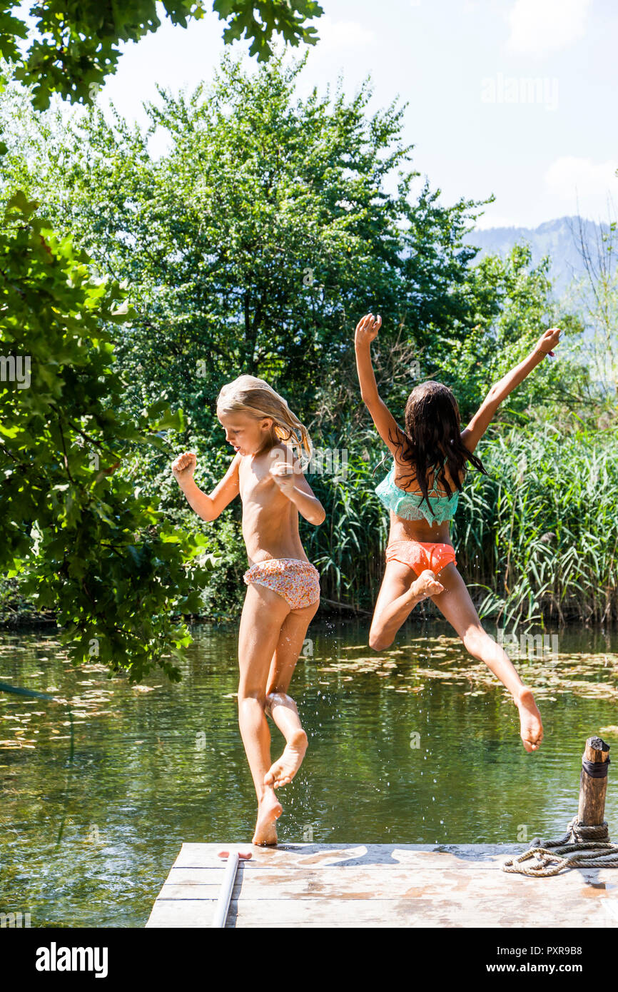 Two carefree girls jumping into pond Stock Photo