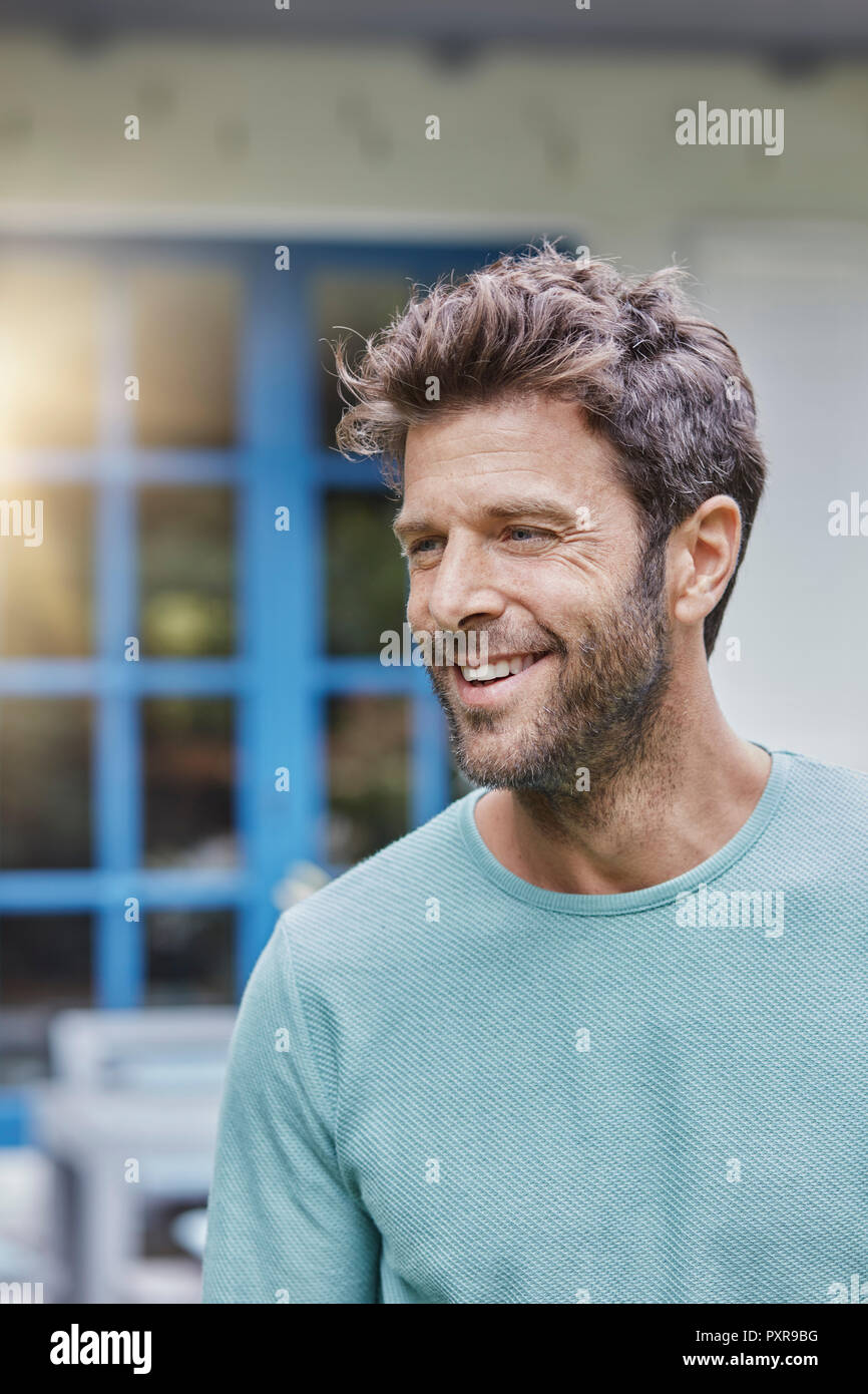 Portrait of smiling man in front of house with blue window Stock Photo