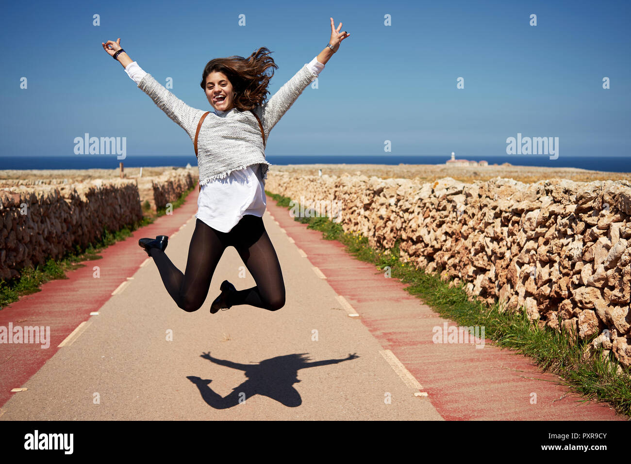 Cheerful young woman jumping in air with rising hands, outdoors Stock Photo