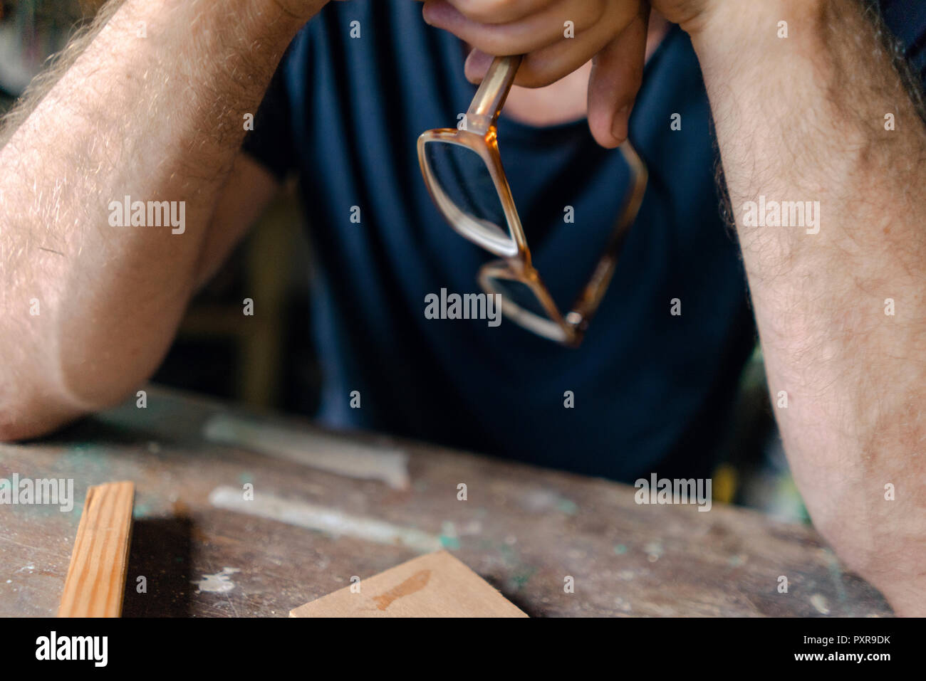 Close-up of man at workbench in workshop holding eyeglasses Stock Photo