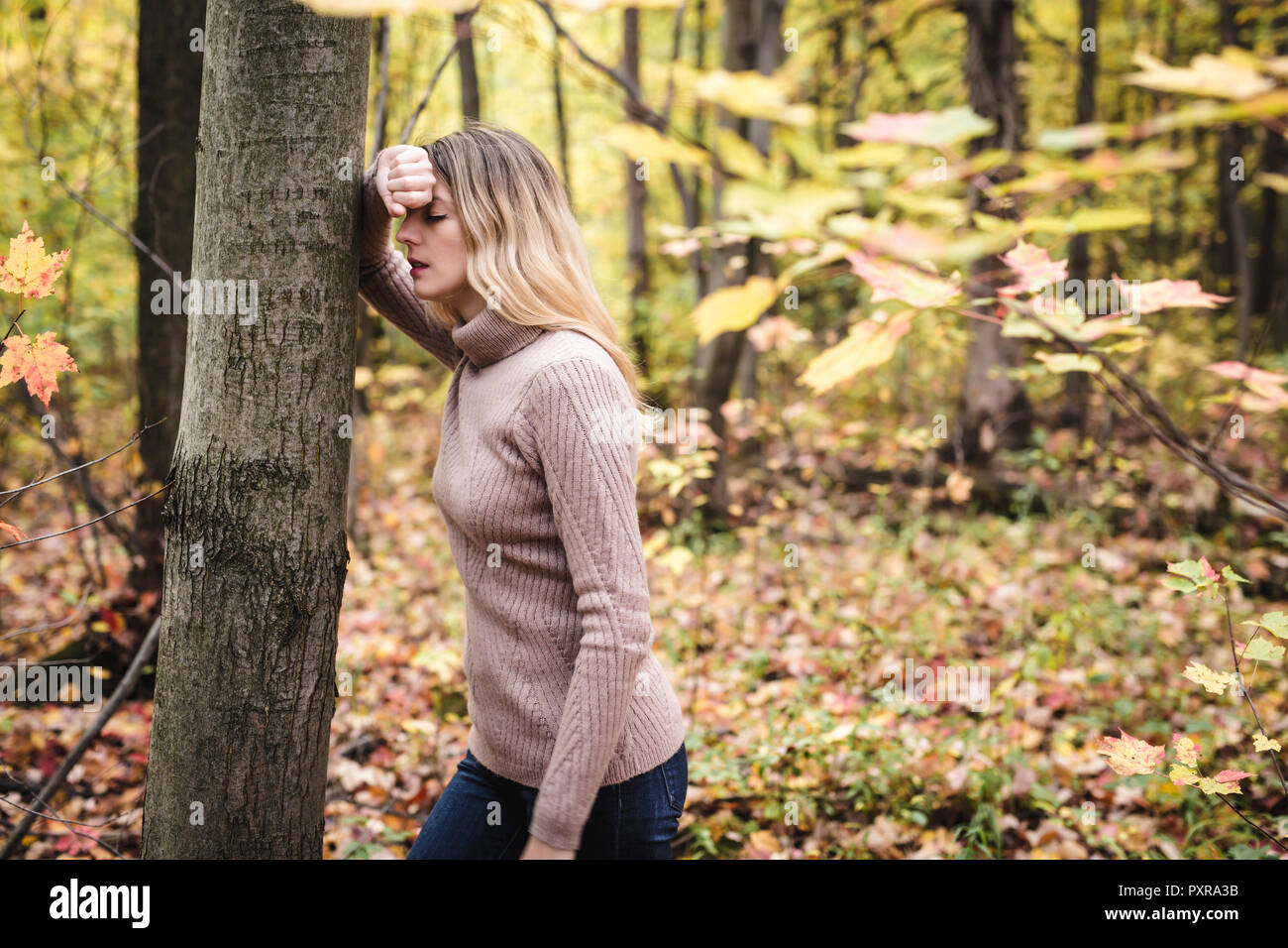 A Sad woman in park during autumn weather hiding face in hand, feeling terrible depressed. Stock Photo