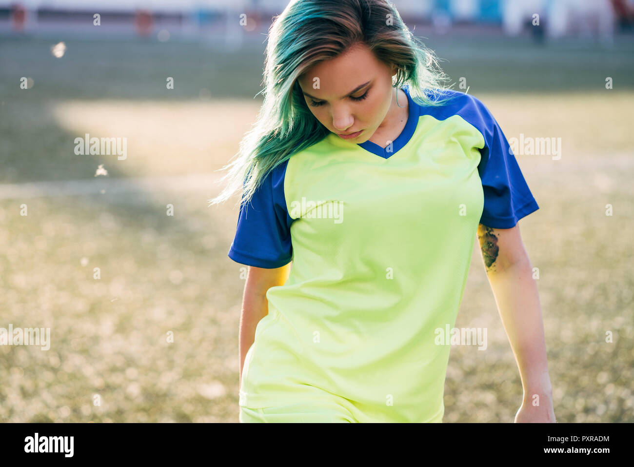 Portrait of young woman in jersey on football ground looking down Stock Photo