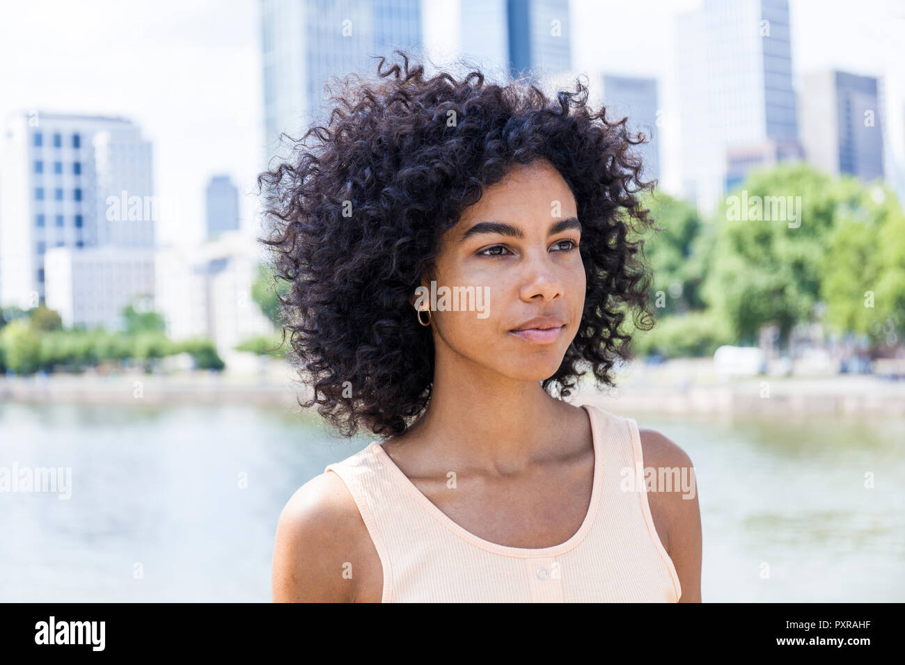 Germany, Frankfurt, portrait of young woman with curly hair in front of Main River Stock Photo