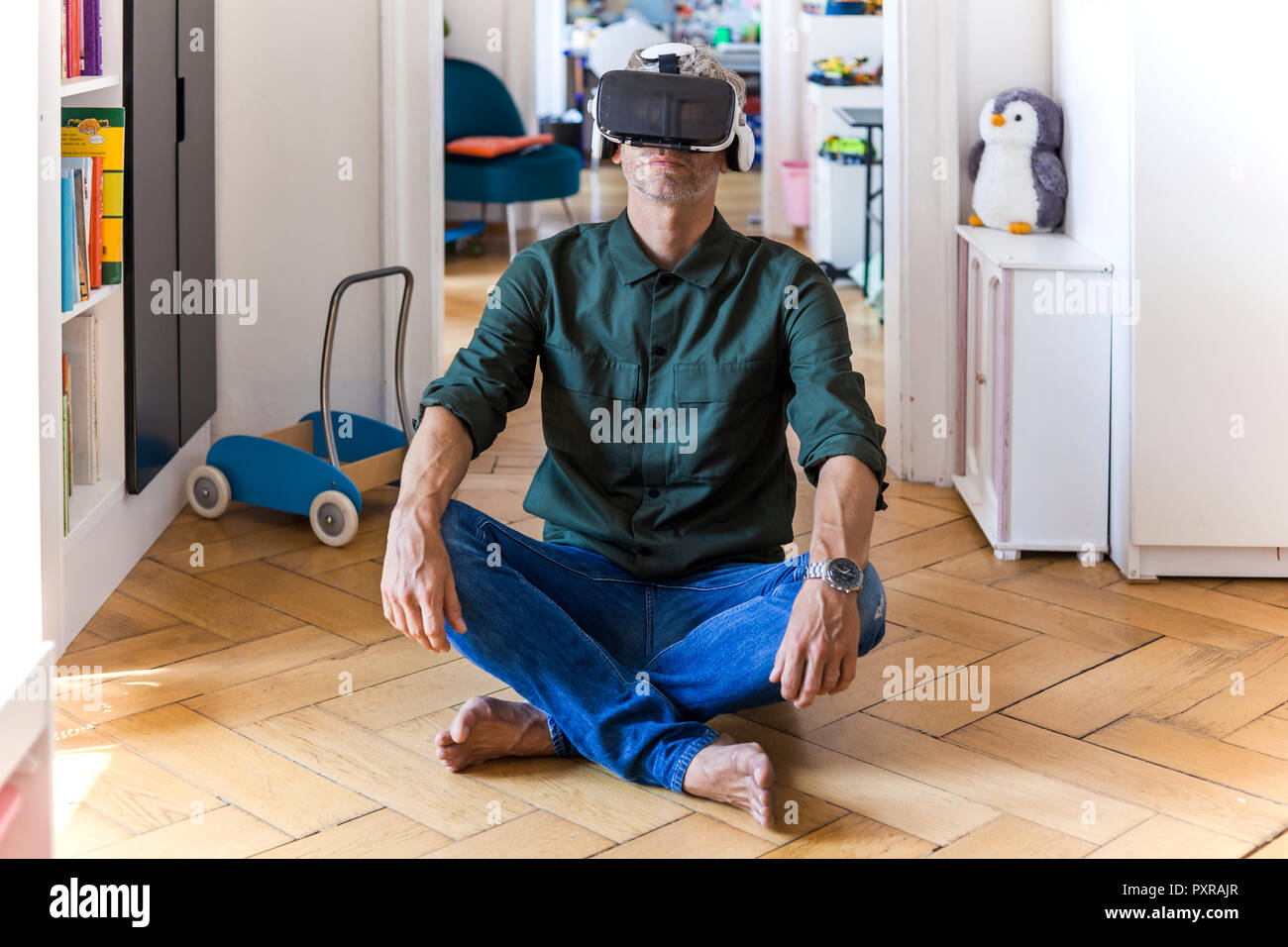 Mature man sitting on the floor at home using Virtual Reality Glasses Stock Photo