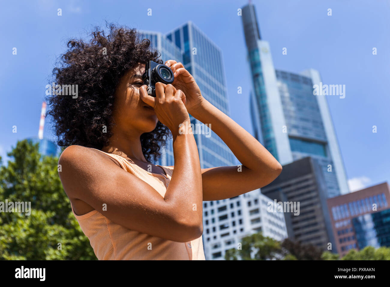 Germany, Frankfurt, young woman with curly hair taking photos in the city Stock Photo