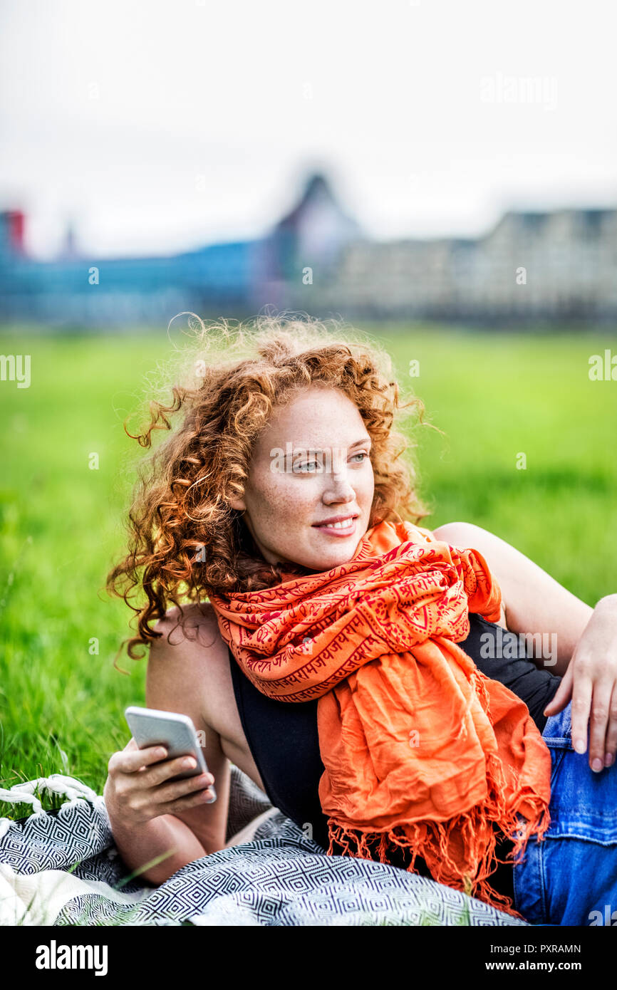 Portrait of smiling young woman with curly red hair wearing orange scarf lying on blanket on a meadow Stock Photo