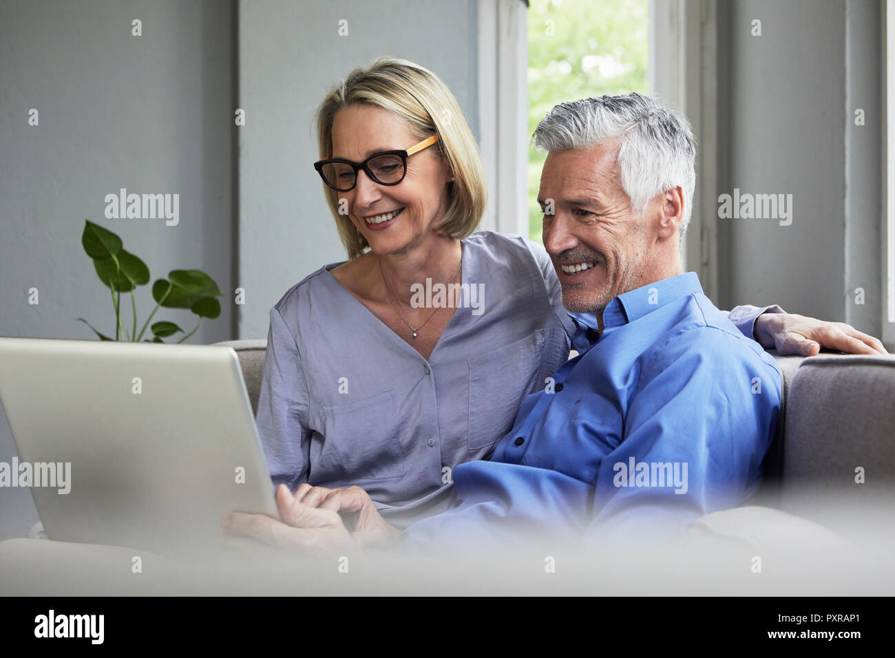Happy mature couple sitting on couch at home sharing laptop Stock Photo