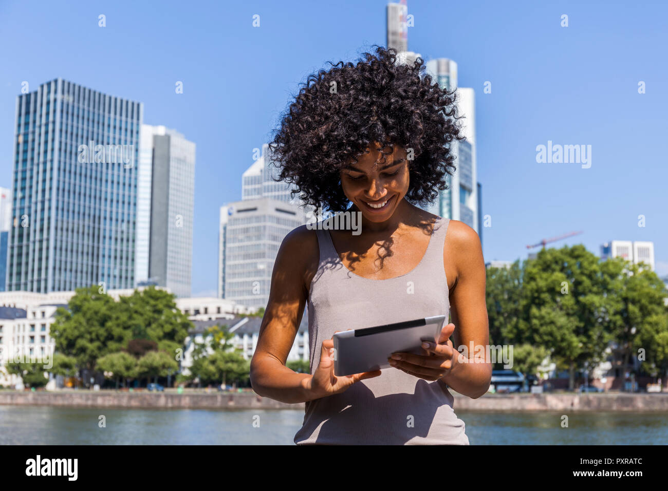 Germany, Frankfurt, smiling young woman with curly hair using tablet in the city Stock Photo