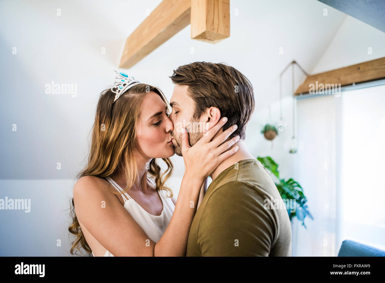 Affectionate couple kissing at home with woman wearing tiara Stock Photo