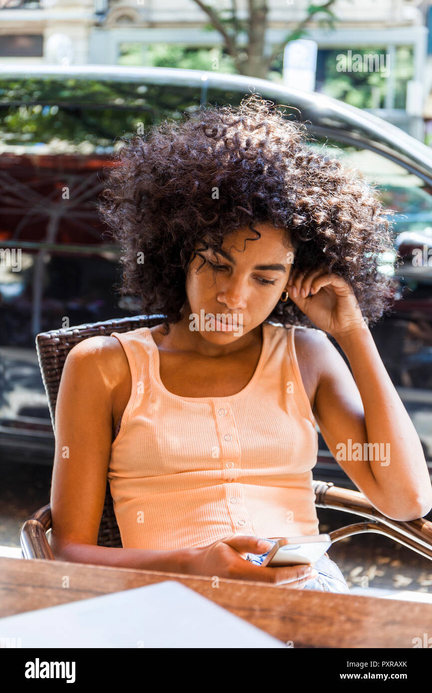 Portrait of young woman with curly hair sitting at sidewalk cafe looking at cell phone Stock Photo