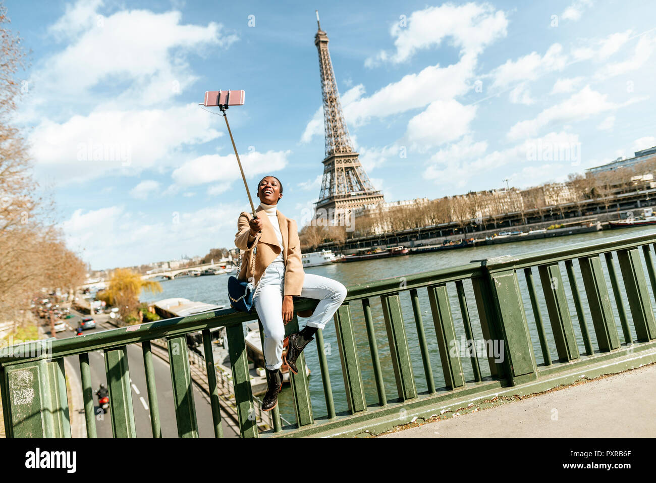 France, Paris, Woman sitting on bridge over the river Seine with the Eiffel tower in the background taking a selfie Stock Photo